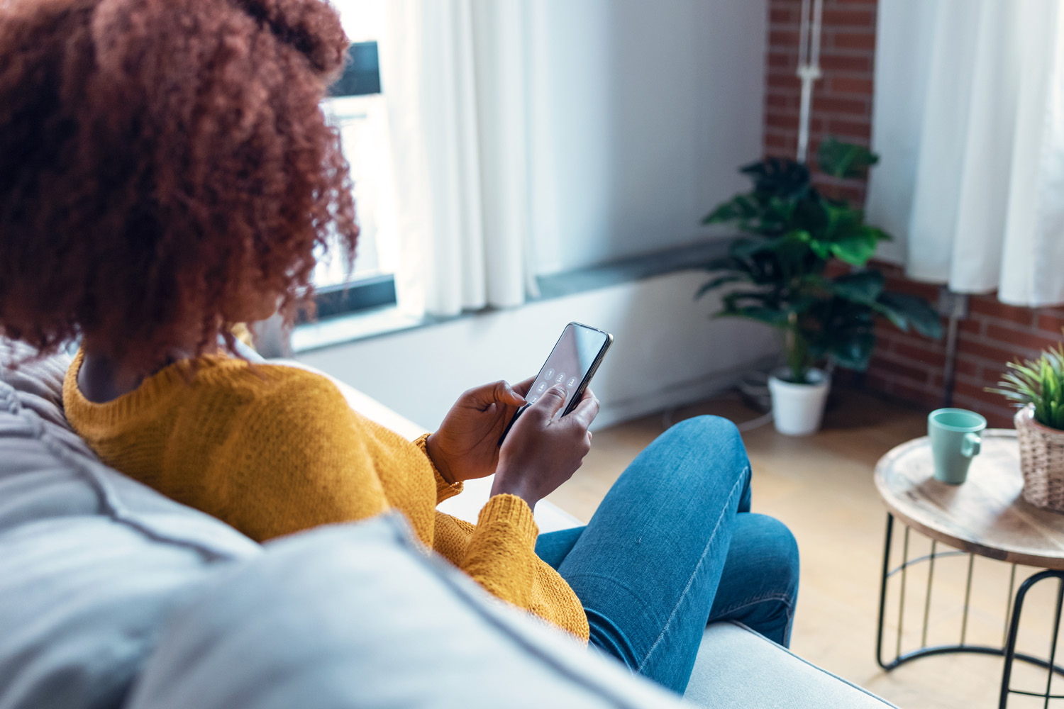 Confident young woman using her mobile phone while sitting on so