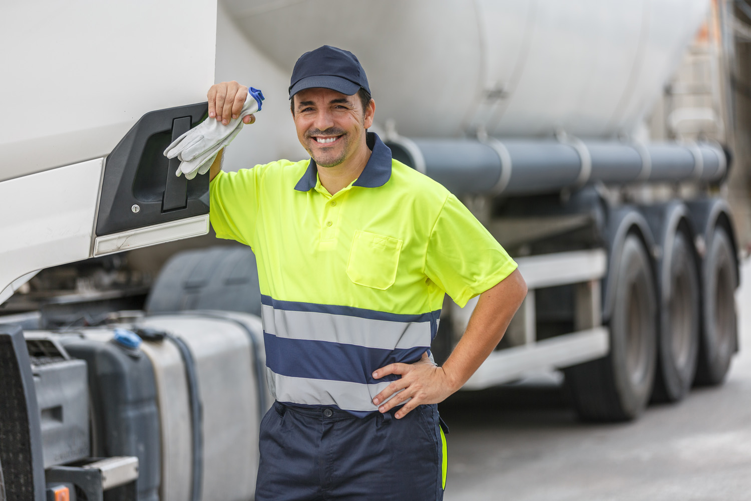 Smiling truck driver standing by vehicle over blurred background Smiling propane tanker driver